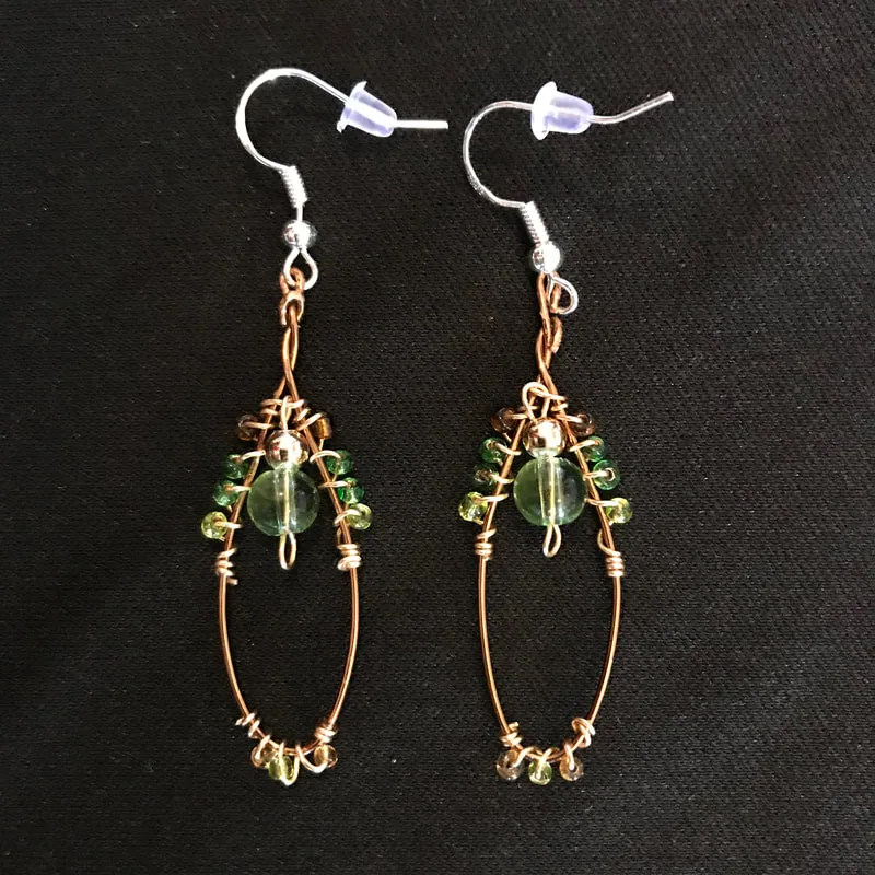 bronze wire shaped into oval earrings with green, brown, and gold beads