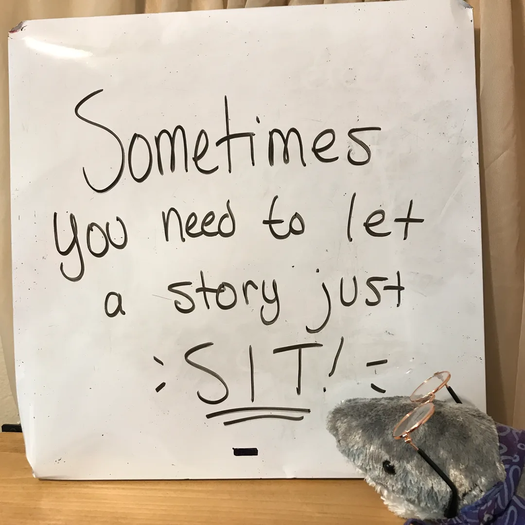 A plush shark with a scarf and glasses sitting in front of a white board with a writing tip written on it